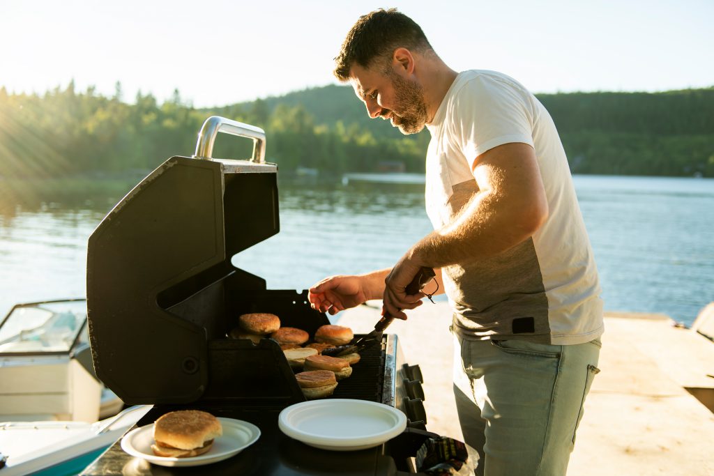 Picture of father preparing hamburger on a grill outdoors close to a lake